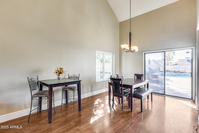 dining room featuring a chandelier, high vaulted ceiling, baseboards, and wood finished floors