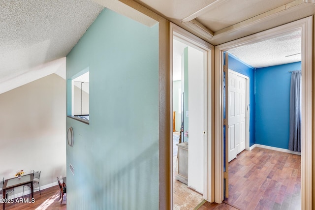 hall featuring a textured ceiling, light wood-style flooring, and baseboards