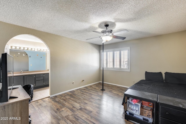 bedroom featuring a textured ceiling, ensuite bathroom, wood finished floors, and baseboards