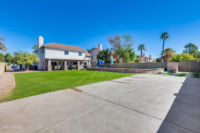 rear view of house featuring stucco siding, a fenced backyard, a chimney, and a yard