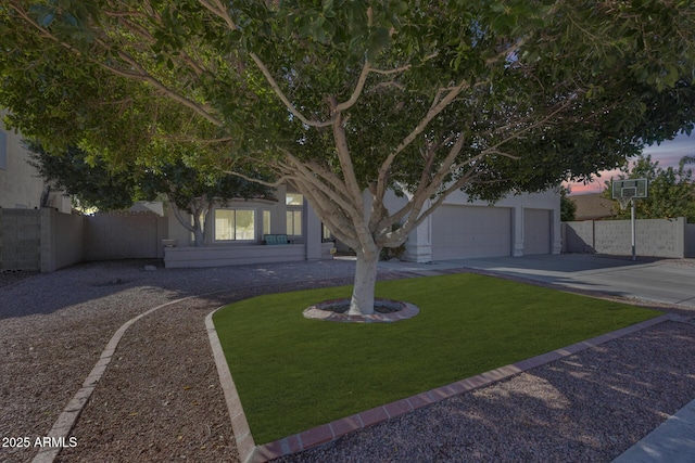 obstructed view of property with concrete driveway, a lawn, fence, and stucco siding