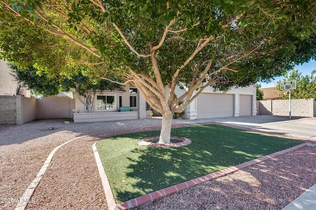 view of property hidden behind natural elements featuring a garage, concrete driveway, stucco siding, fence, and a front yard