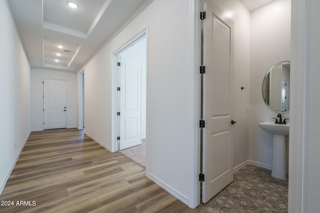 hall with light hardwood / wood-style floors and a raised ceiling