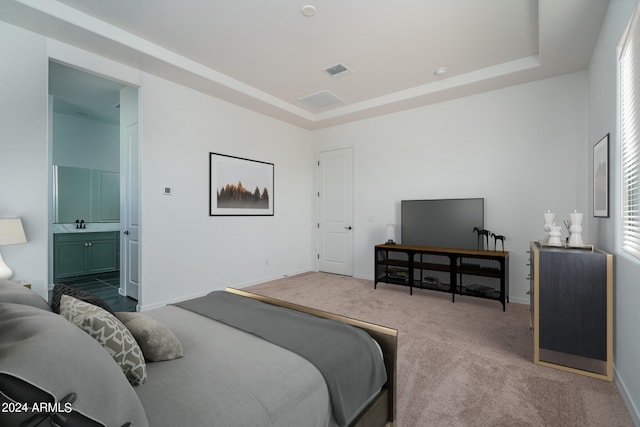 carpeted bedroom featuring ensuite bathroom and a raised ceiling