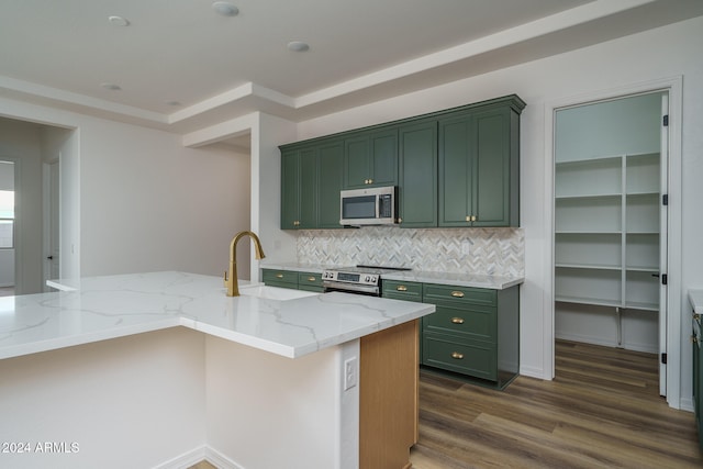 kitchen with a center island with sink, stainless steel appliances, green cabinets, light stone countertops, and dark hardwood / wood-style flooring