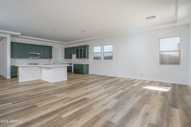 kitchen with an island with sink, tasteful backsplash, green cabinetry, hardwood / wood-style flooring, and crown molding