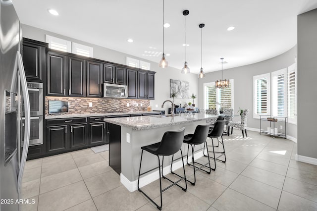 kitchen featuring pendant lighting, appliances with stainless steel finishes, a kitchen island with sink, a kitchen breakfast bar, and light stone counters