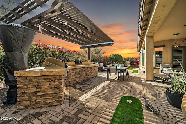 patio terrace at dusk featuring an outdoor kitchen and a pergola