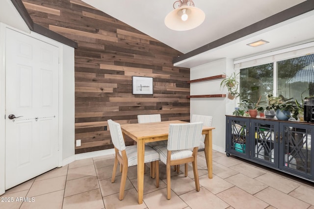 dining room with wooden walls, light tile patterned floors, high vaulted ceiling, and baseboards