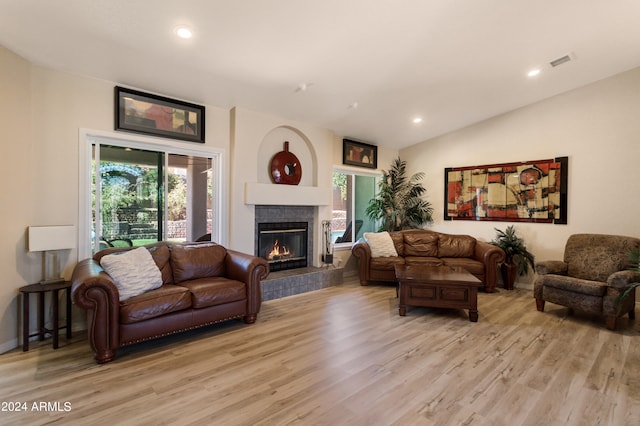 living room with lofted ceiling, a tiled fireplace, and light hardwood / wood-style flooring