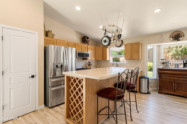 kitchen with appliances with stainless steel finishes, lofted ceiling, light wood-type flooring, and a notable chandelier