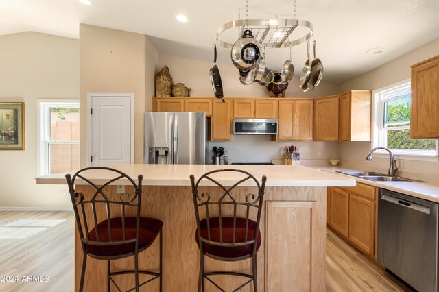 kitchen featuring appliances with stainless steel finishes, vaulted ceiling, a kitchen island, light wood-type flooring, and sink