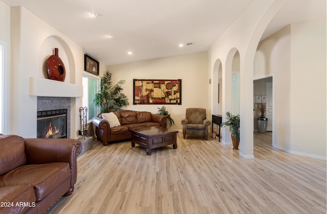 living room featuring light hardwood / wood-style flooring, lofted ceiling, and a tiled fireplace