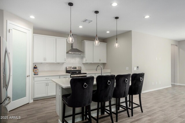 kitchen featuring stainless steel appliances, light countertops, white cabinetry, an island with sink, and wall chimney exhaust hood