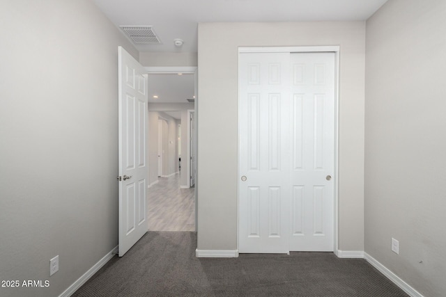 unfurnished bedroom with a closet, visible vents, dark carpet, and baseboards