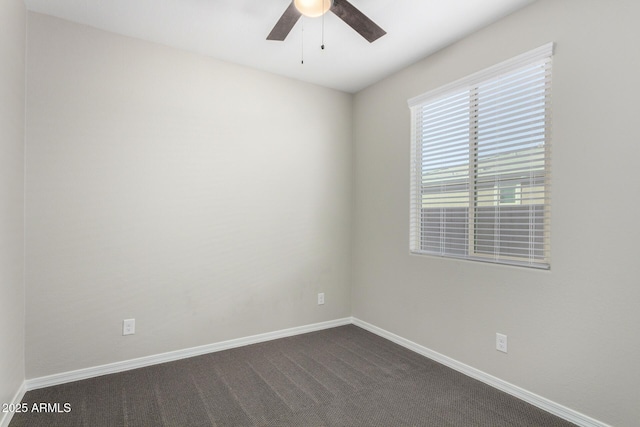 empty room featuring dark colored carpet, a ceiling fan, and baseboards