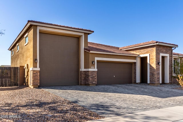 prairie-style house featuring stone siding, an attached garage, fence, decorative driveway, and stucco siding