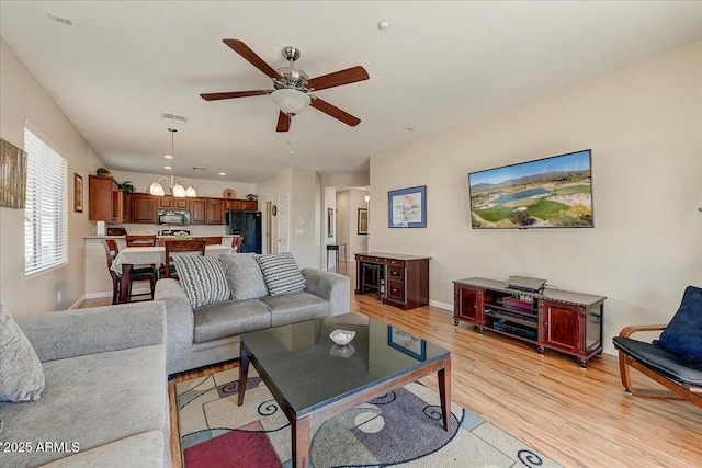 living room featuring ceiling fan with notable chandelier and light hardwood / wood-style floors