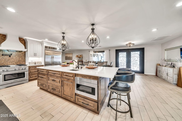 6215 E Surrey Ave, Scottsdale, AZ 85254 - kitchen featuring built in appliances, custom exhaust hood, light countertops, a kitchen breakfast bar, and french doors
