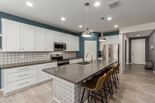 kitchen featuring sink, backsplash, white cabinetry, an island with sink, and stainless steel appliances