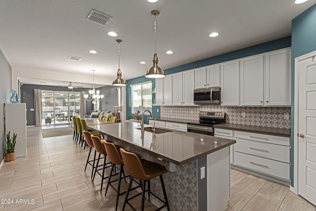 kitchen with appliances with stainless steel finishes, white cabinetry, sink, pendant lighting, and a center island with sink