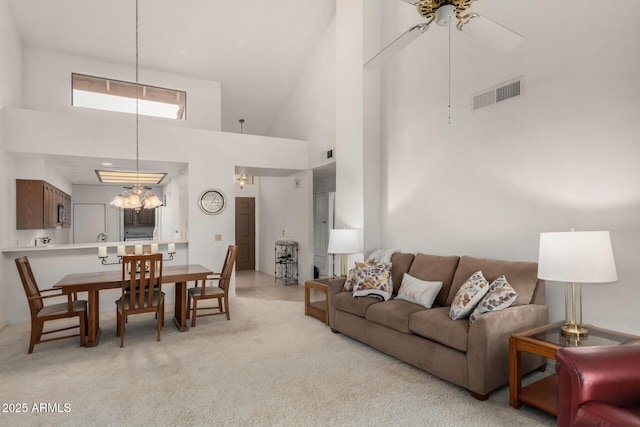 living area with light colored carpet, visible vents, ceiling fan, and a towering ceiling