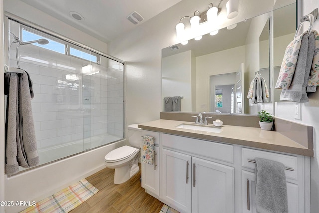 full bath featuring visible vents, toilet, wood finished floors, bath / shower combo with glass door, and vanity