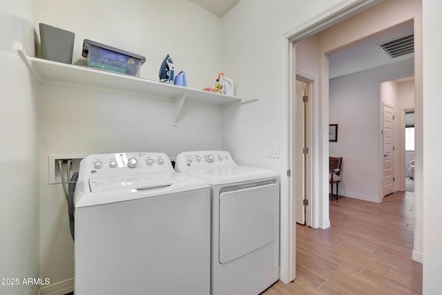 clothes washing area with washer and dryer, light wood-type flooring, baseboards, and visible vents