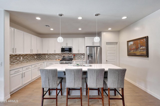 kitchen featuring an island with sink, tasteful backsplash, white cabinetry, stainless steel appliances, and light countertops