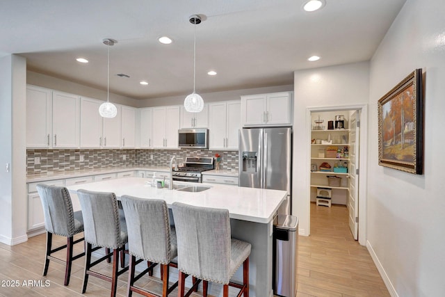 kitchen featuring a breakfast bar, light wood-style flooring, an island with sink, stainless steel appliances, and white cabinets
