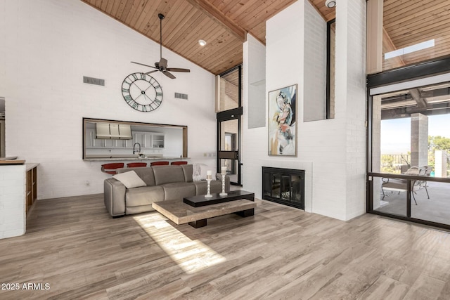 living room with high vaulted ceiling, wood ceiling, light wood-style flooring, and a glass covered fireplace