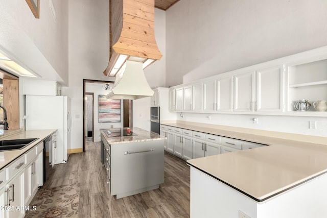 kitchen featuring a sink, light countertops, a center island, dishwashing machine, and a high ceiling