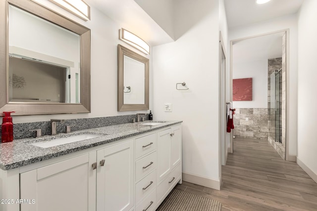 full bathroom with wood finished floors, a tile shower, double vanity, and a sink