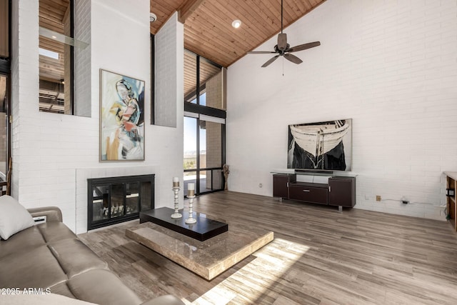 living area featuring wooden ceiling, wood finished floors, ceiling fan, a glass covered fireplace, and high vaulted ceiling