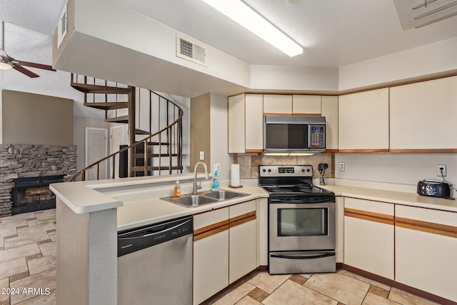 kitchen with kitchen peninsula, stainless steel appliances, ceiling fan, sink, and a stone fireplace