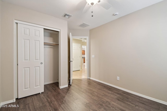 unfurnished bedroom with baseboards, visible vents, dark wood finished floors, and a closet