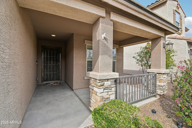 view of exterior entry with a porch, stone siding, and stucco siding