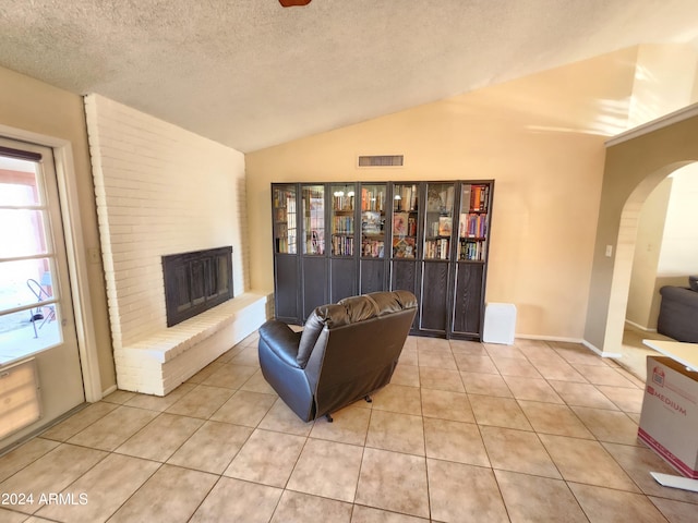 sitting room with light tile patterned flooring, a fireplace, vaulted ceiling, and a textured ceiling