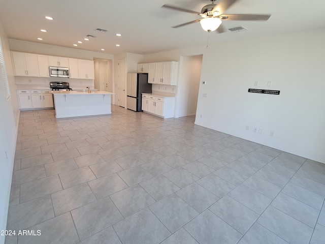 kitchen with stainless steel appliances, ceiling fan, white cabinets, an island with sink, and light tile patterned flooring