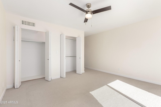 unfurnished bedroom with light carpet, two closets, and ceiling fan