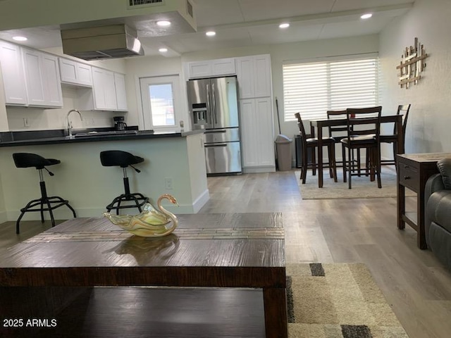 kitchen with white cabinetry, stainless steel fridge with ice dispenser, exhaust hood, and light wood-type flooring