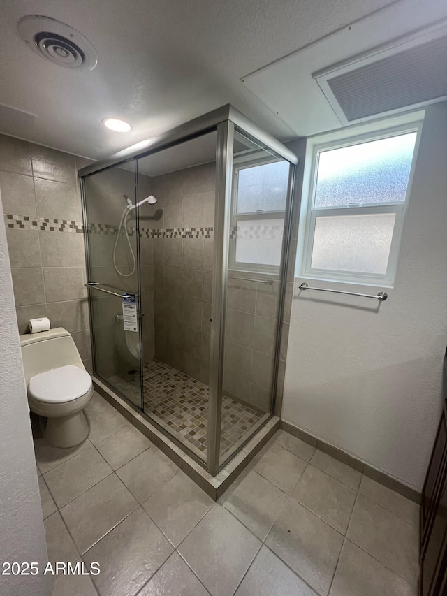 bathroom with tile patterned flooring, a shower with shower door, and toilet