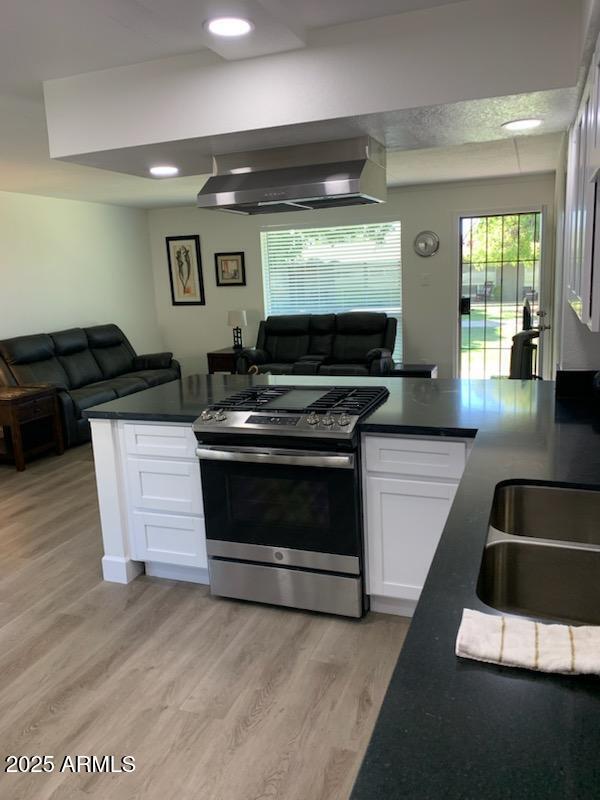 kitchen with white cabinetry, light wood-type flooring, stainless steel range with gas cooktop, and wall chimney range hood