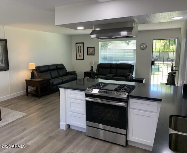 kitchen with wall chimney exhaust hood, white cabinets, light hardwood / wood-style floors, and stainless steel gas range