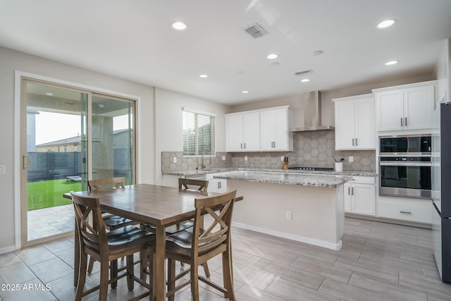 kitchen featuring light stone counters, wall chimney range hood, white cabinets, and a kitchen island