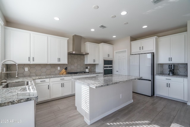 kitchen with built in microwave, sink, white fridge, stainless steel oven, and wall chimney range hood