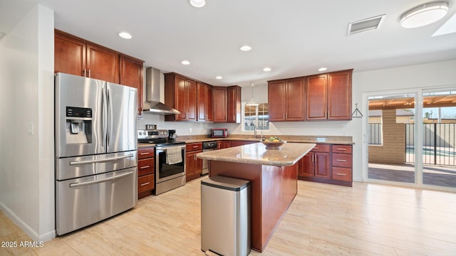 kitchen featuring wall chimney exhaust hood, decorative light fixtures, a kitchen island, stainless steel appliances, and light stone countertops