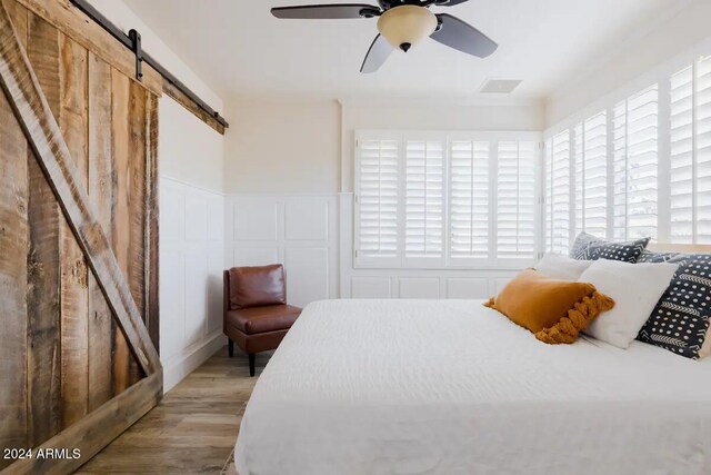 bedroom featuring a barn door, light hardwood / wood-style floors, and ceiling fan