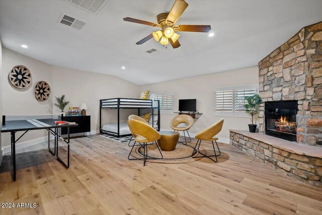 interior space with vaulted ceiling, ceiling fan, light wood-type flooring, and a stone fireplace