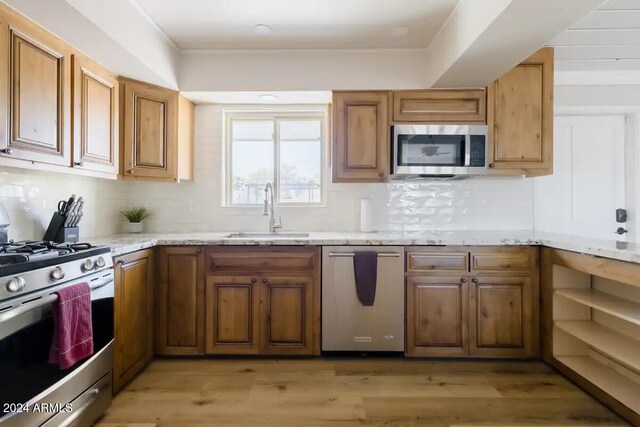 kitchen featuring light stone counters, sink, light hardwood / wood-style floors, and appliances with stainless steel finishes